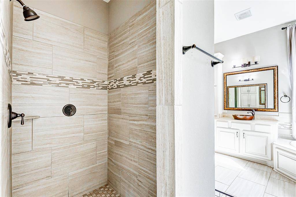 Next, step into the walk-in shower, featuring a neutral tile surround complemented by accent tiles and elegant bronze finishes, creating a tranquil and sophisticated bathing experience.