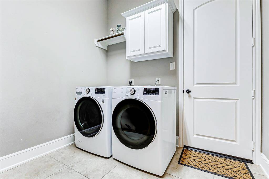 The expansive laundry room boasts neutral tile flooring, washer connections, and a built-in cabinet with a shelf and hanging rack for added convenience.