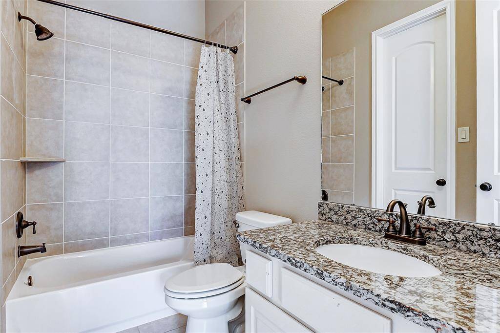 The guest bathroom features a vanity with sleek granite countertops, complemented by bronze finishes, and a tub/shower combination.