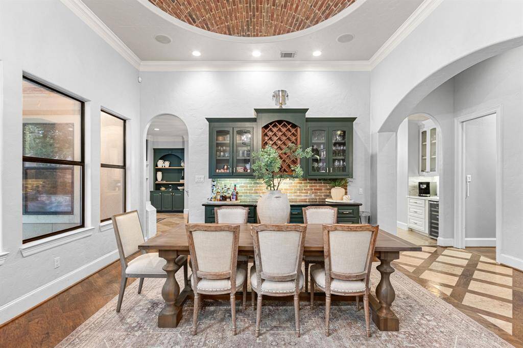 Elegant dining area features a brick ceiling accent, a built-in custom cabinet with glass doors. The space is brightened by large windows and an open layout, creating a warm and inviting atmosphere.