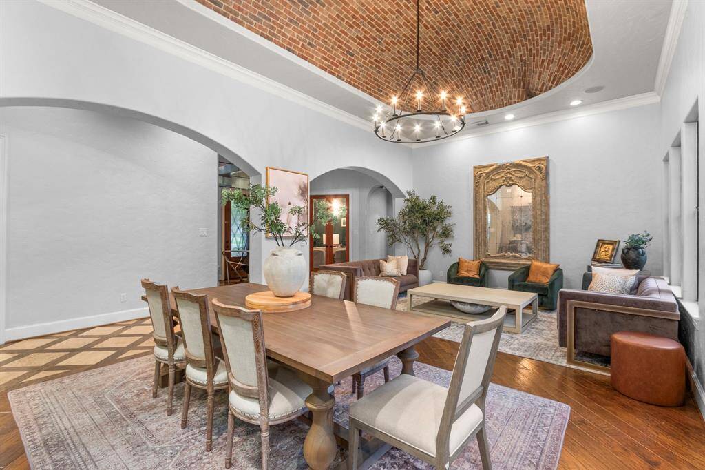 Elegant dining/living room features a high, barrel-vaulted brick ceiling with a central chandelier. It combines a dining area with a spacious sitting area. Arched doorways and large windows enhance the open, airy feel.