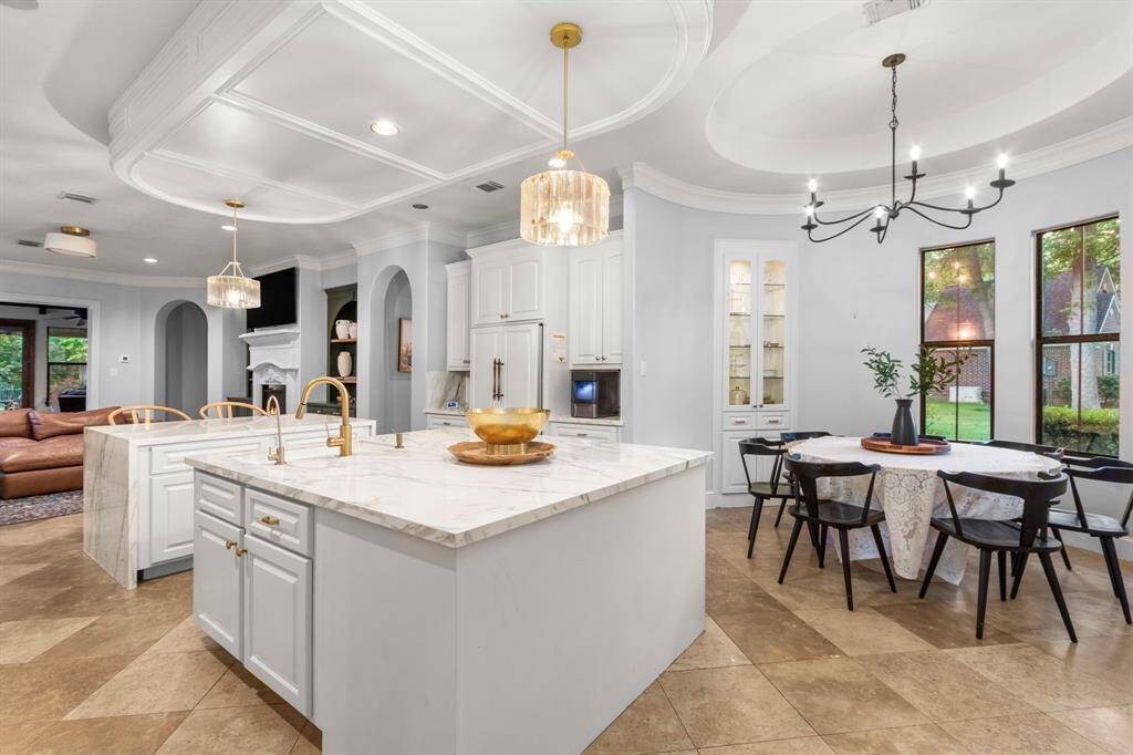 Spacious and elegant chef's kitchen with porcelain countertops, white cabinetry, and gold fixtures. The open-plan design seamlessly connects cozy dining and living spaces with large windows to the great outdoors.