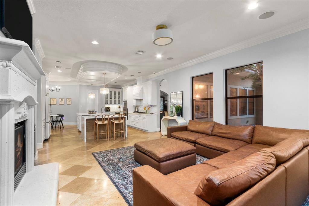 Open-concept living space features  a stone fireplace, open to elegant kitchen with a large island and modern lighting. The area is bright and spacious, perfect for entertaining or relaxing.