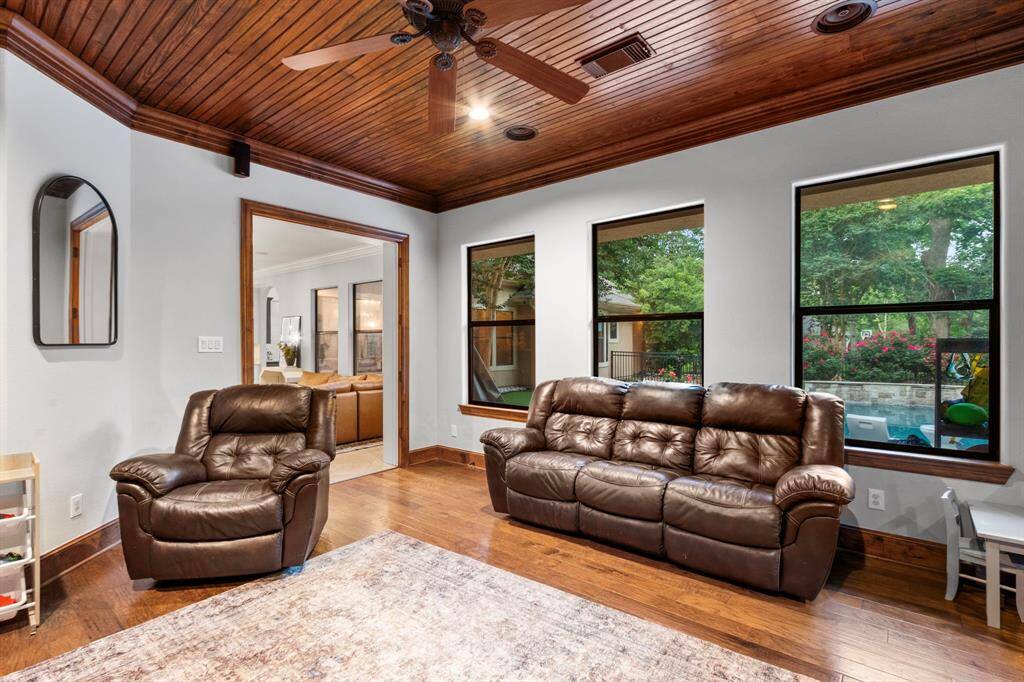This cozy living room features rich wooden floors and ceiling. The large windows offer natural light and views of the beautiful backyard. The space connects seamlessly to another room, enhancing the open feel.