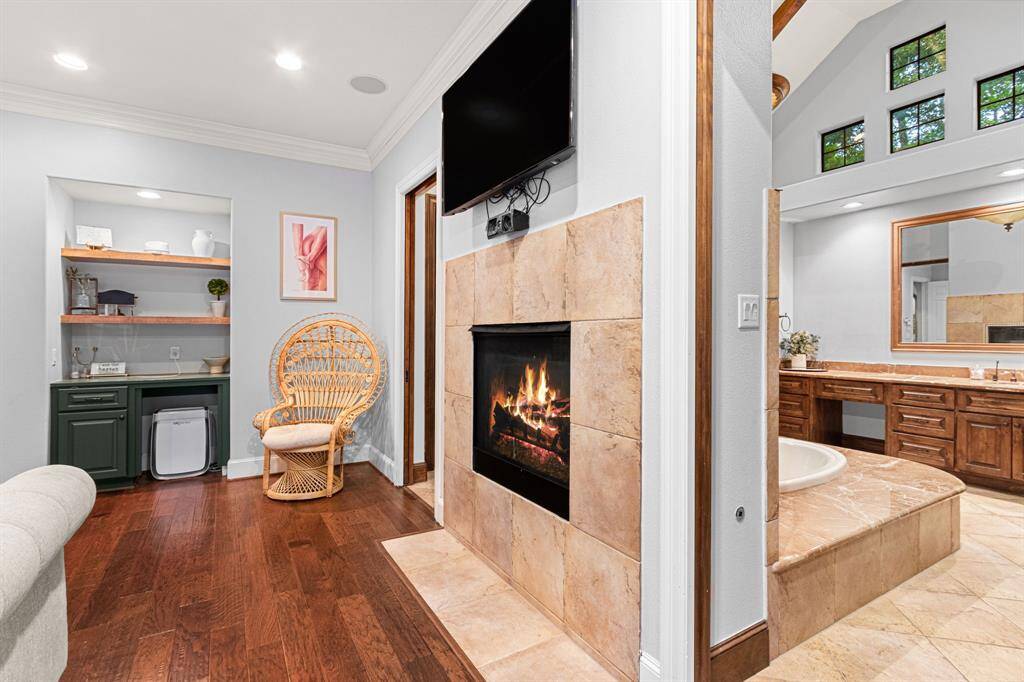 Cozy primary features a warm fireplace, and rich hardwood floors. Adjacent is a luxurious bathroom with a large tub and elegant cabinetry, topped with high ceilings and ample natural light from upper windows.