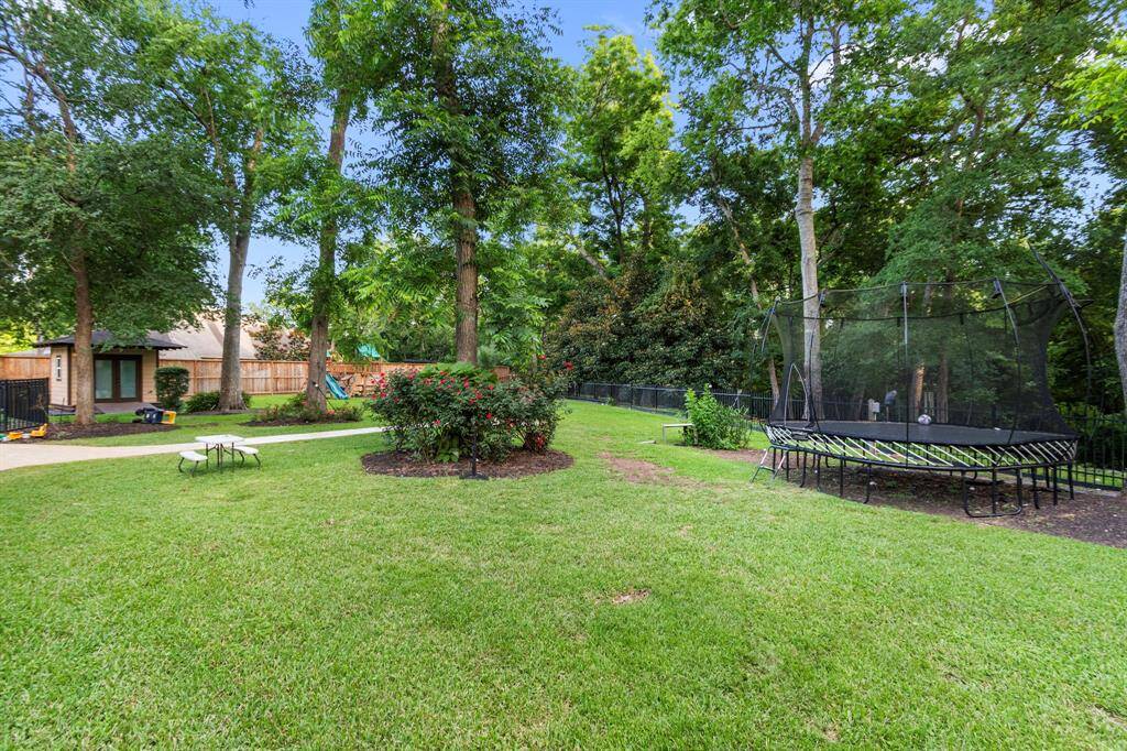 Spacious backyard with lush greenery, featuring a trampoline and a play area. Ideal for families, it offers a serene outdoor space with mature trees and a small garden. Perfect for relaxation and outdoor activities.