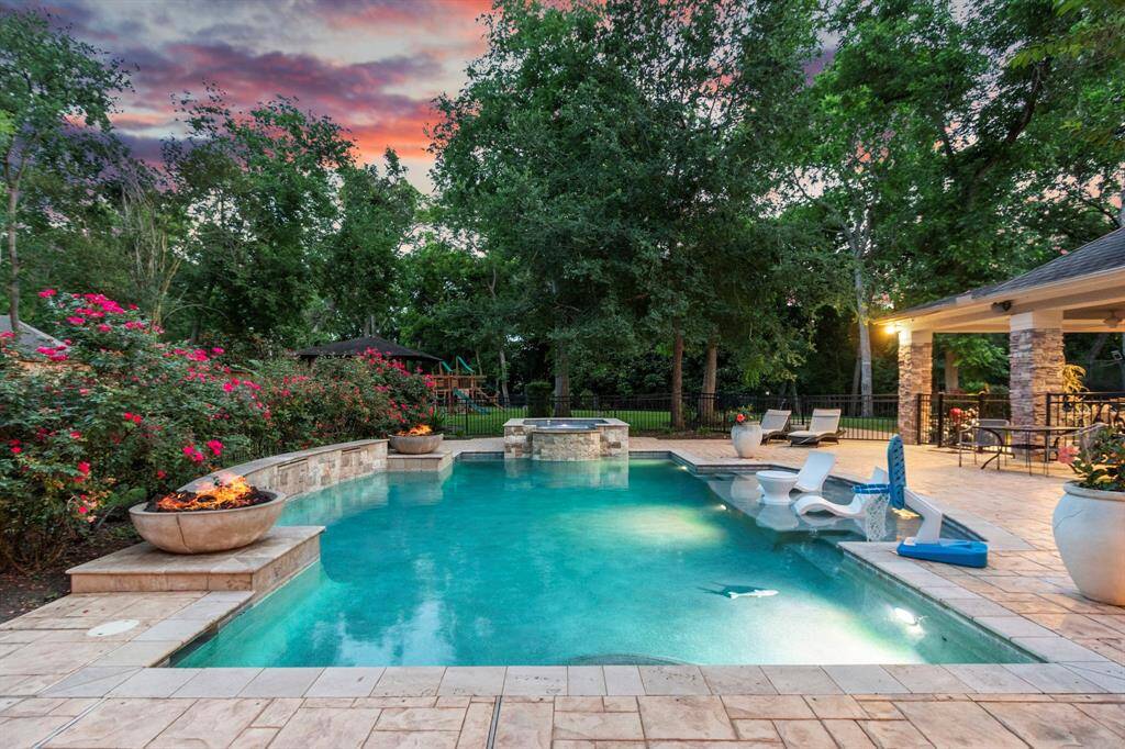 This photo showcases a luxurious backyard with a sparkling pool and waterfall hot tub. There is a cozy outdoor living patio area  ideal for relaxation and entertaining.