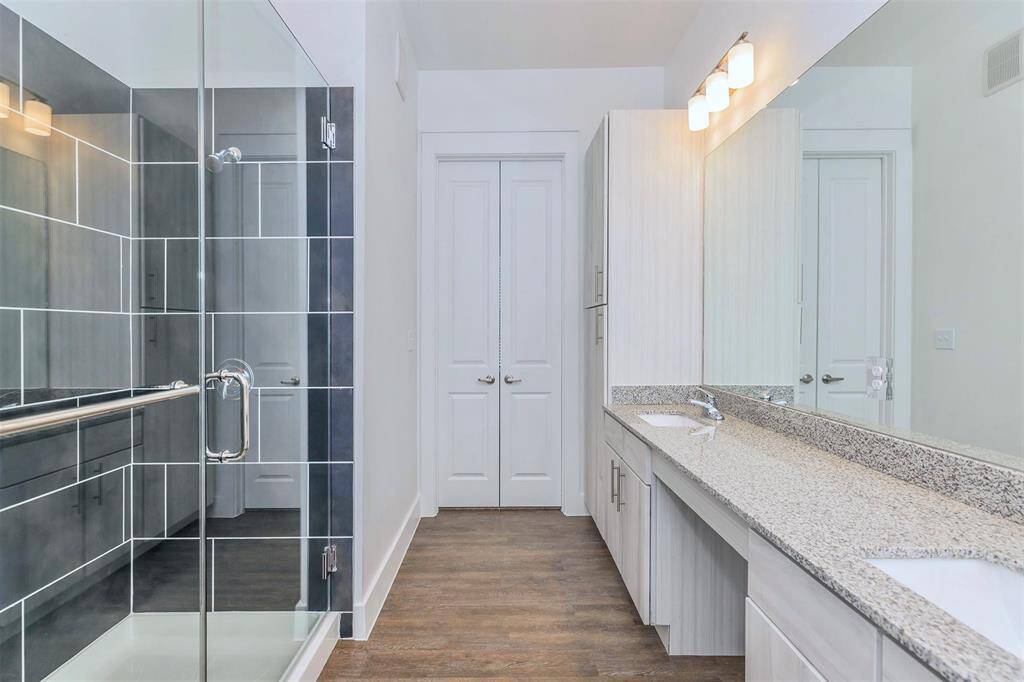 Spacious bathroom with double sinks, walk-in shower, modern finishes, and granite countertops