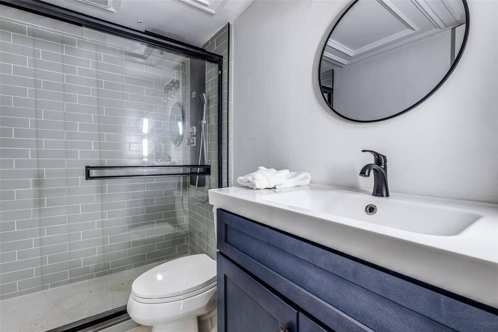 .Large glass-enclosed shower with modern shower fixtures , framed mirror and a stylish blue vanity with updated counters.