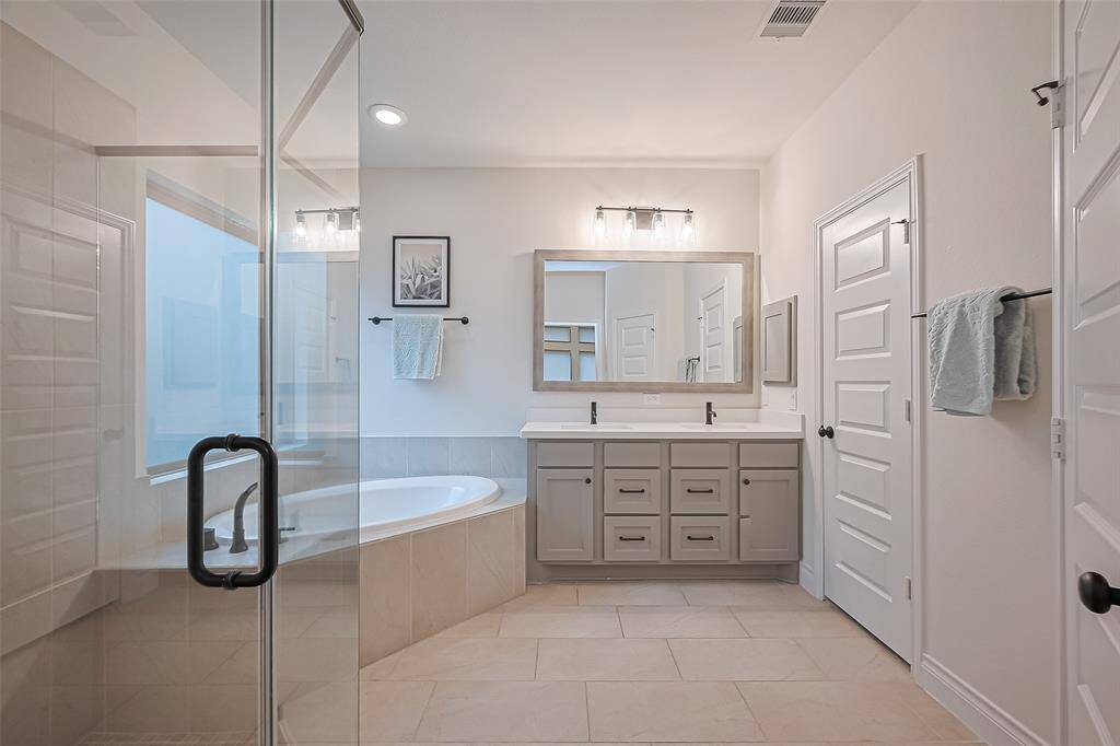Double doors lead into a spa-inspired en suite bathroom, where you'll find a corner soaking tub, a walk-in glass-enclosed shower, dual vanities with framed mirrors, a medicine cabinet, and a generously sized walk-in closet outfitted with built-in shelving and ample hanging space.