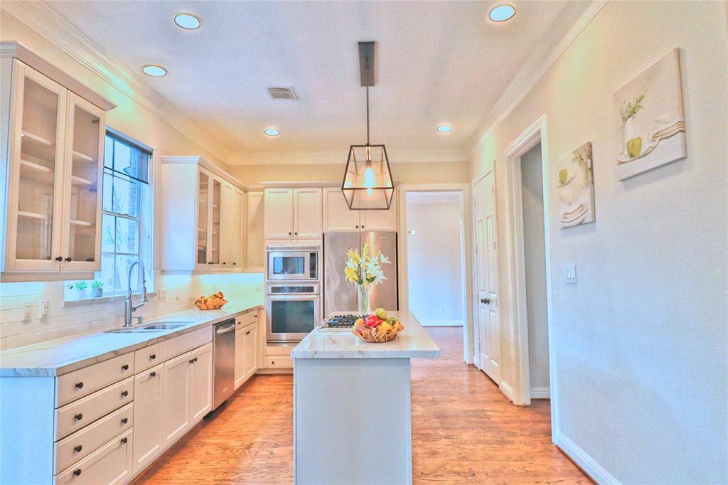 This kitchen features a modern design and a central island with pendant lighting. It has hardwood floors, ample counter space, and large windows for natural light.