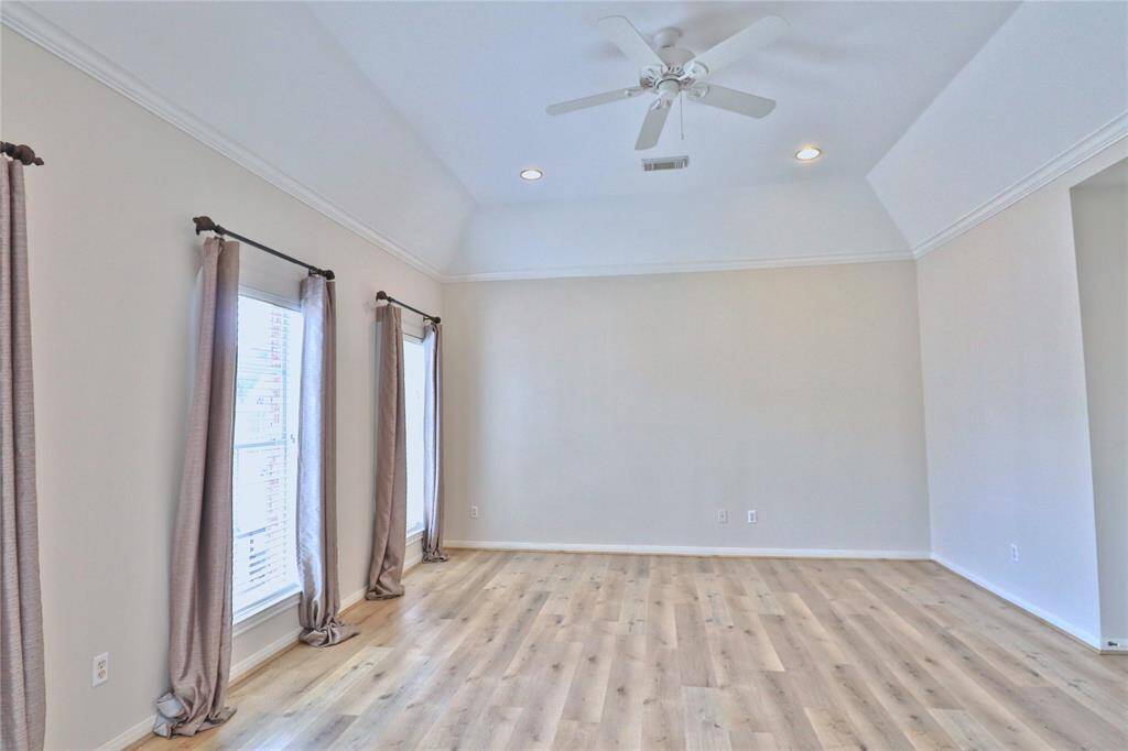 Bright, spacious primary room with high ceilings and recessed lighting. Features large windows with curtains, and a ceiling fan, creating an airy and inviting atmosphere.