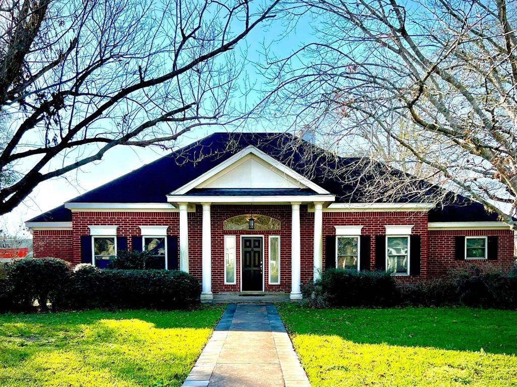 This beautifully maintained single-story brick home features a welcoming front porch, classic columns, and a manicured lawn framed by mature trees, creating an inviting first impression.