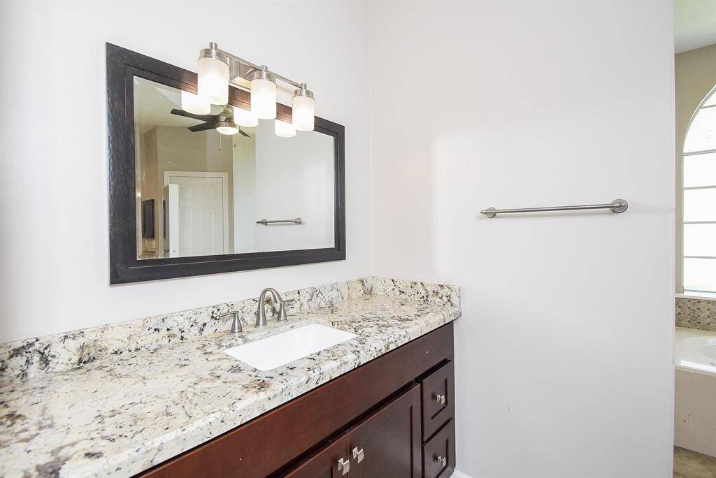 A refined bathroom with a granite countertop vanity, modern fixtures, and an elegant mirror, offering a spa-like experience