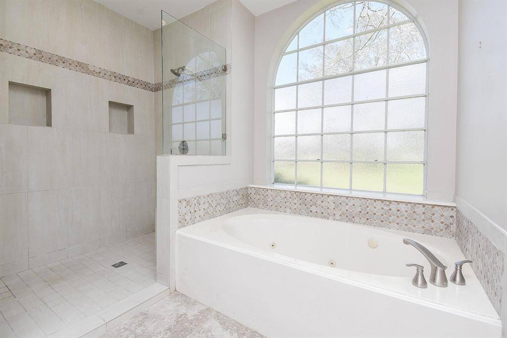 A luxurious soaking tub beneath a large arched window, perfect for unwinding in a peaceful and serene bathroom retreat.