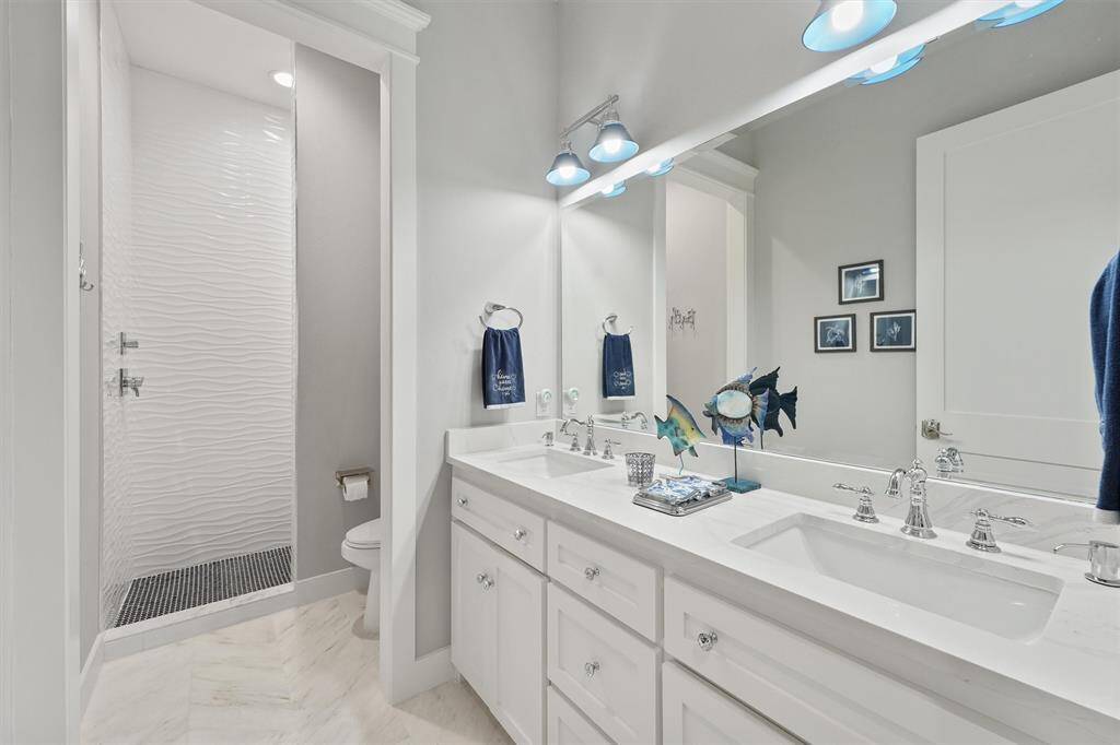 Sleek and bright full bath featuring dual sinks, modern lighting, ample counter space, and elegant tile flooring--designed for both comfort and functionality