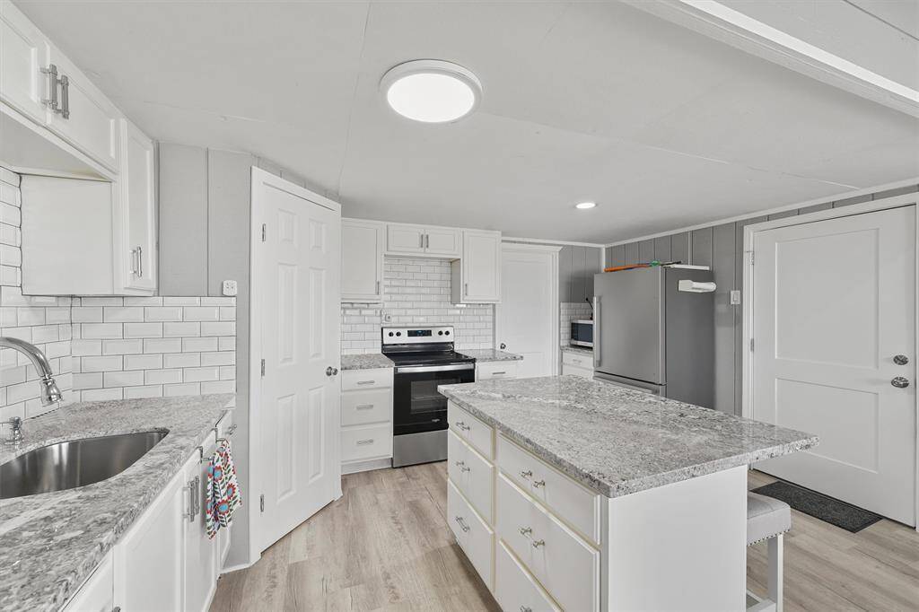 Full equipped downstairs kitchen featuring granite countertops, subway tile backsplash, stainless steel appliances, and a center island with seating