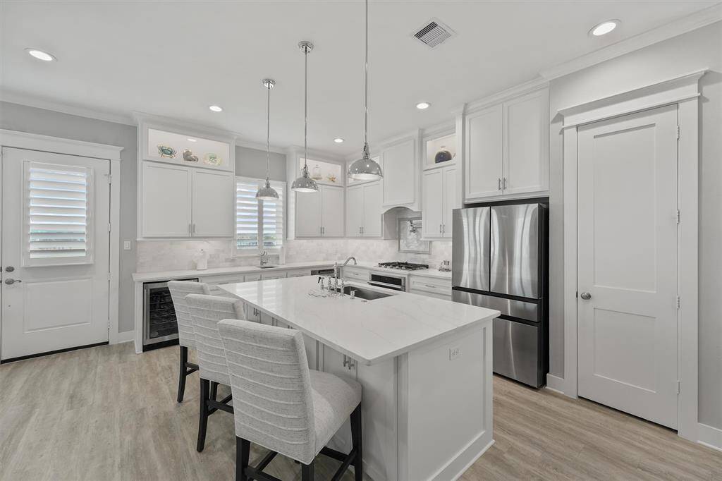 This angle highlights the expansive island with bar seating, perfect for casual dining or entertaining.Crisp white cabinetry, marble backsplash, and quartz countertops are complemented by premium stainless appliances, dual dishwashers, Wifi enabled gas cooktop with pot filler.