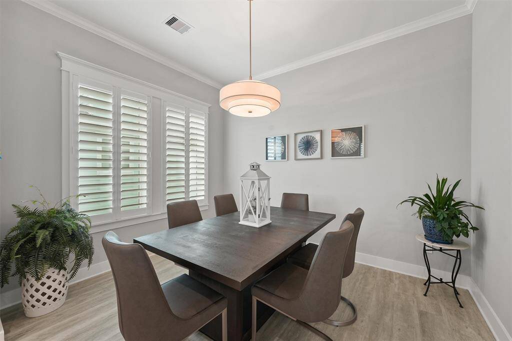Framed by plantation shutters and soft natural light, this elegant dining space blends coastal charm with modern sophistication. Crown molding and designer lighting elevate the ambiance, creating the perfect setting