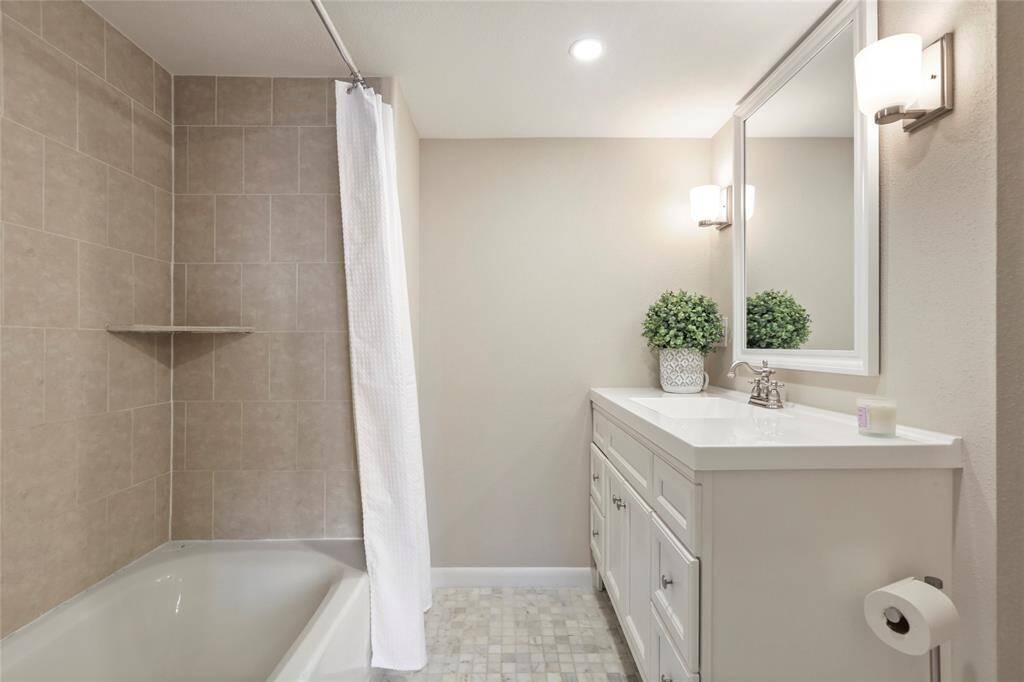 Luxurious primary bath featuring a bathtub/shower combo, elegant tilework, a modern vanity, and soft lighting for a serene retreat.