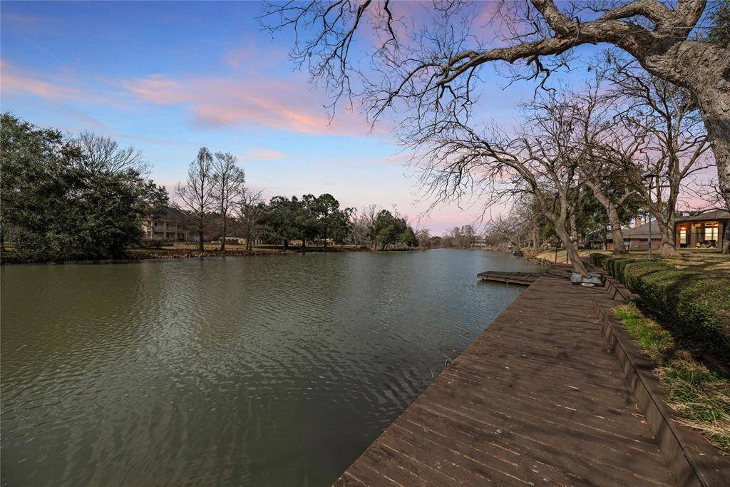This serene lakeside view features a wooden dock along calm waters, bordered by lush trees and a picturesque sky, offering a peaceful and inviting setting.