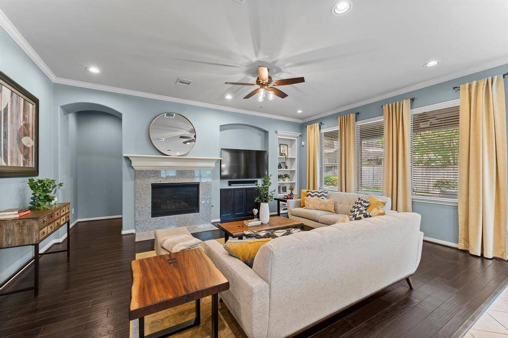 This cozy yet spacious family room showcases a modern design with large windows, recessed lighting, crown moldingm built-in shelving, and a fireplace, all seamlessly open to the kitchen and breakfast room.