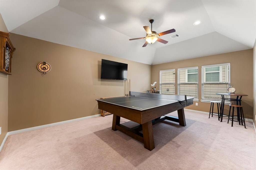 The spacious game room features vaulted ceilings and abundant natural light from a wall of windows. Perfectly suited for entertainment, it also offers flexible space for a playroom, or hobby area.