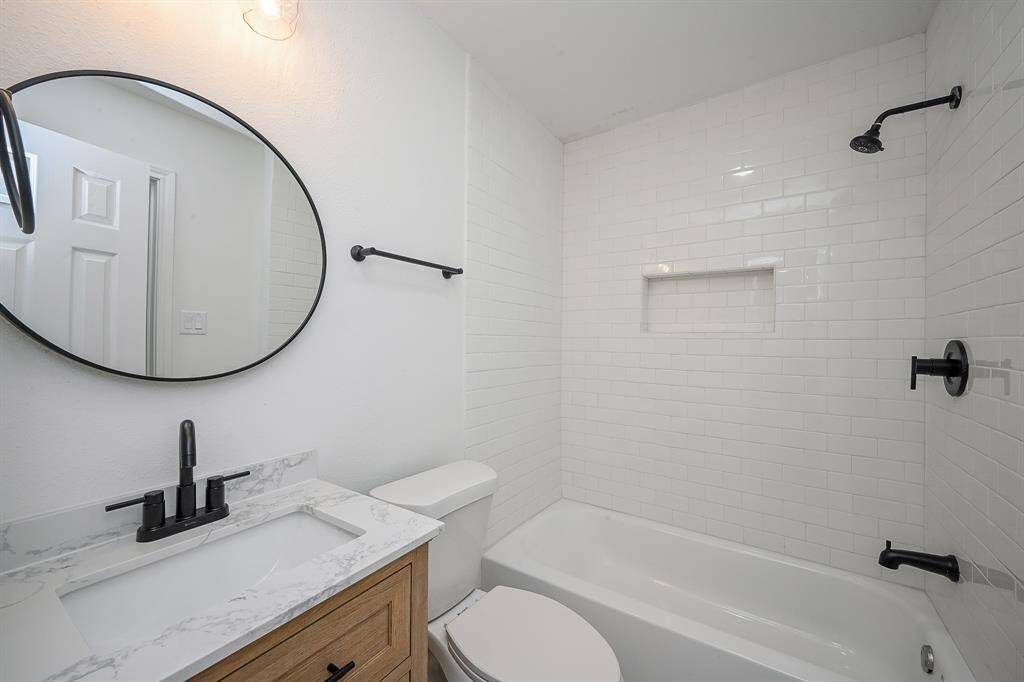 Bathroom with quartz countertops and backsplash, wooden cabinetry, and a shower/tub combo.