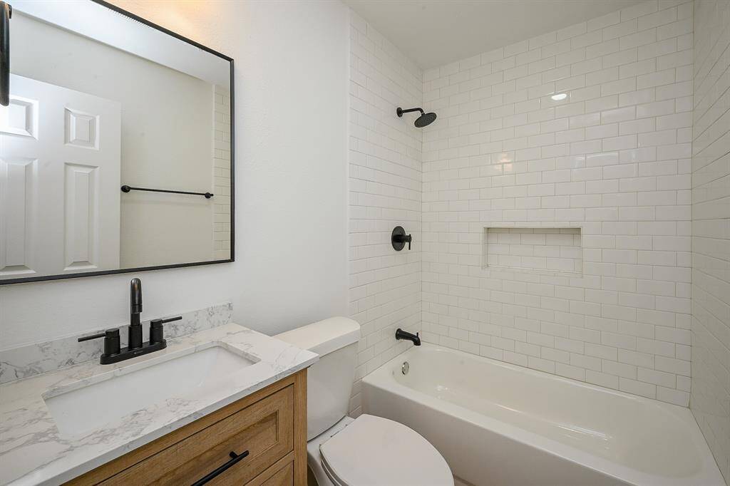 Bathroom with quartz countertops and backsplash, wooden cabinetry, and a shower/tub combo.