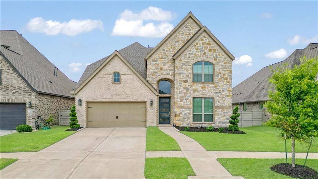 Charming two-story home with a stone and brick exterior, featuring a spacious driveway and a two-car garage. Well-maintained lawn and modern front door design add to its curb appeal.