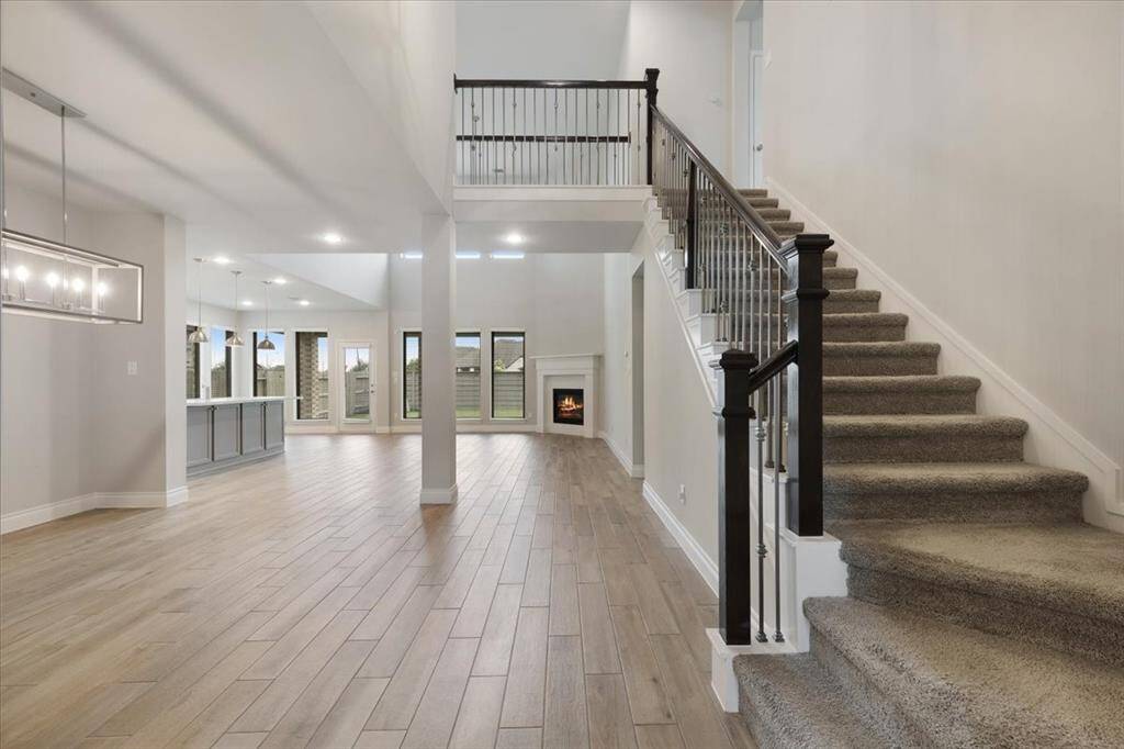 This spacious home features an open floor plan with a sleek, modern staircase, hardwood floors, and ample natural light. The living area includes a cozy fireplace, and the adjacent kitchen boasts a large island and contemporary lighting.