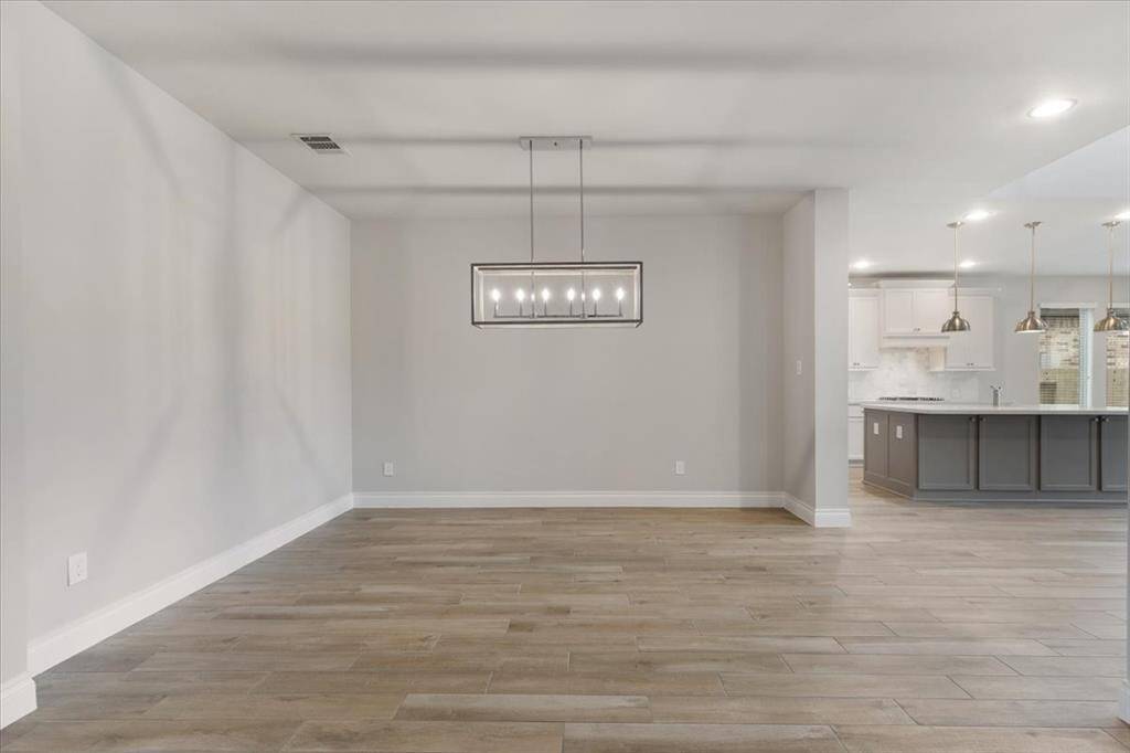 This photo showcases a modern open-concept dining and kitchen area. The space features light wood flooring, a sleek rectangular chandelier, and a contemporary kitchen with an island and pendant lighting. The neutral color palette enhances the room's spacious and inviting feel.