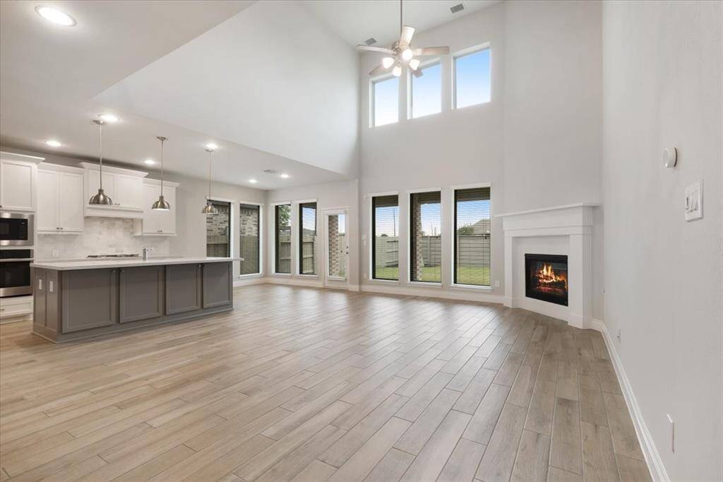 This spacious living area features high ceilings, large windows for natural light, a cozy corner fireplace, and an open-concept kitchen with modern appliances and an island. Perfect for entertaining and family gatherings.