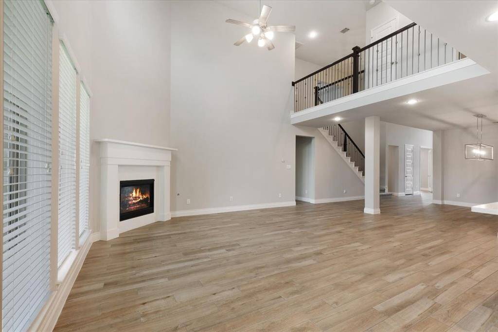 This spacious living area features high ceilings, a cozy fireplace, and large windows for natural light. The open layout includes a modern staircase leading to a loft area, with sleek hardwood floors throughout. Perfect for a bright and inviting home atmosphere.