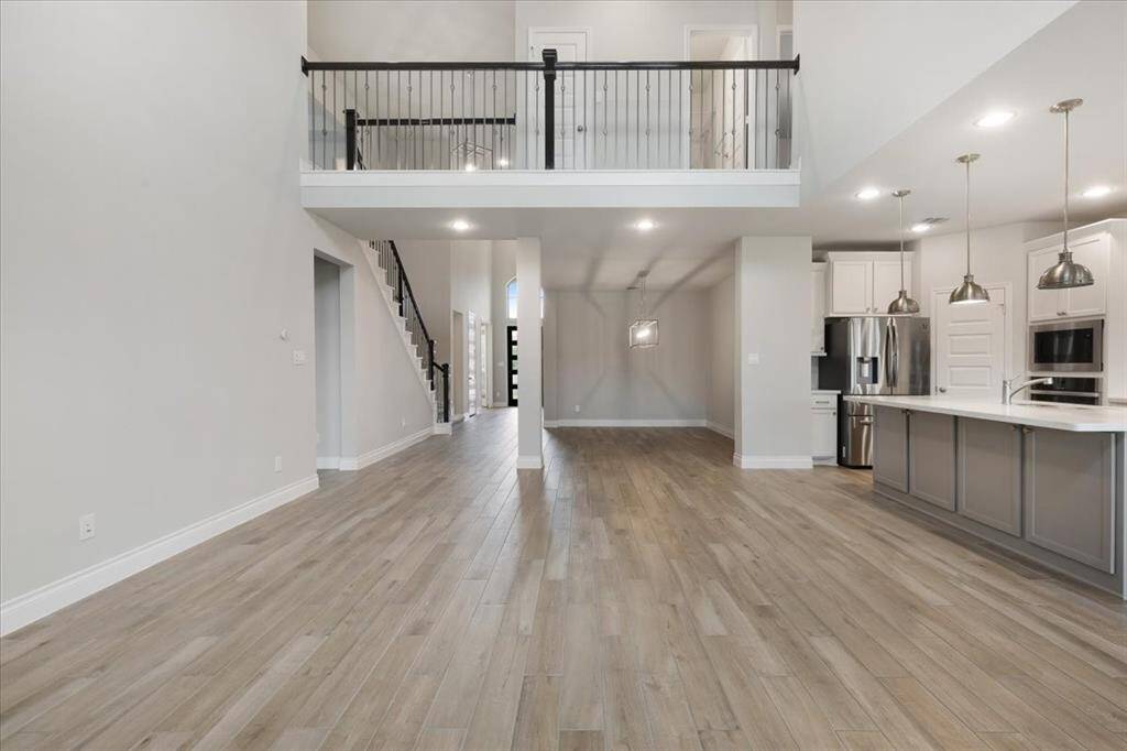 This spacious home features an open-concept living area with high ceilings and a modern kitchen. Hardwood floors run throughout, and the upstairs loft overlooks the main floor. The kitchen includes contemporary lighting, stainless steel appliances, and a large island, perfect for entertaining.