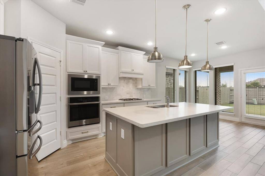 This modern kitchen features a spacious island with pendant lighting, sleek stainless steel appliances, and ample natural light from large windows, offering a bright and inviting space.