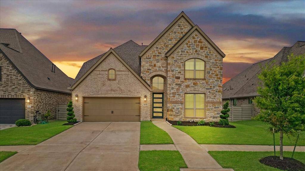 This photo showcases a beautiful two-story stone and brick house with a neatly manicured lawn and a double garage. The evening sky adds a warm backdrop, highlighting the home's elegant exterior and inviting ambiance.