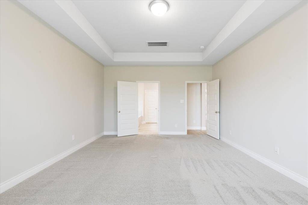 This room features neutral walls and carpet, a tray ceiling with a central light fixture, and two doors, offering a spacious and versatile area for customization.