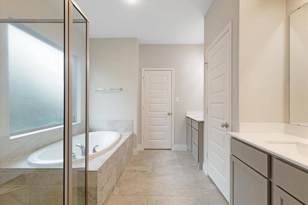 This spacious bathroom features a large soaking tub, a glass-enclosed shower, modern cabinetry, and ample counter space, all in a neutral color palette for a serene atmosphere.