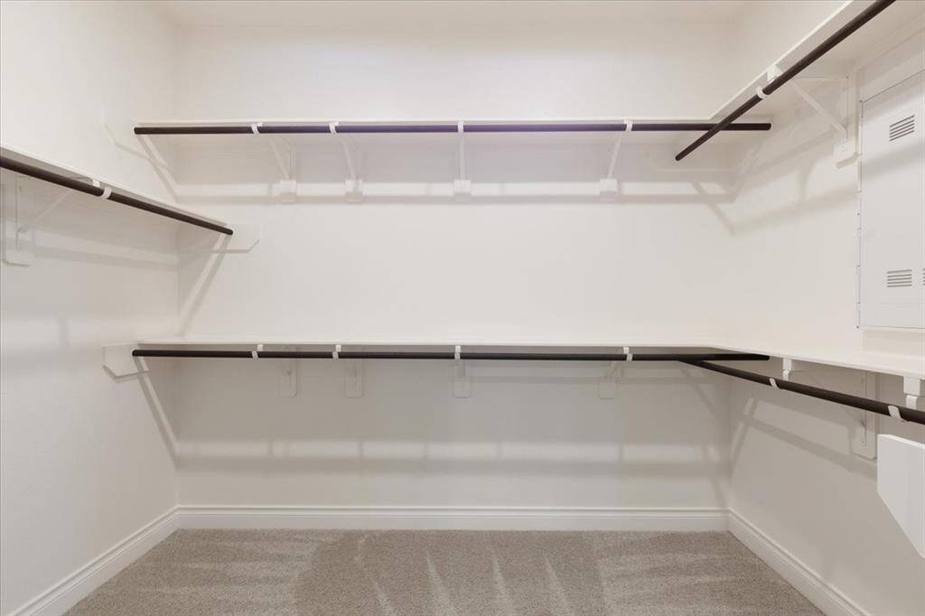 This photo shows a spacious walk-in closet with multiple shelves and hanging rods, offering ample storage space. The neutral tones and carpeted floor provide a clean, organized look.