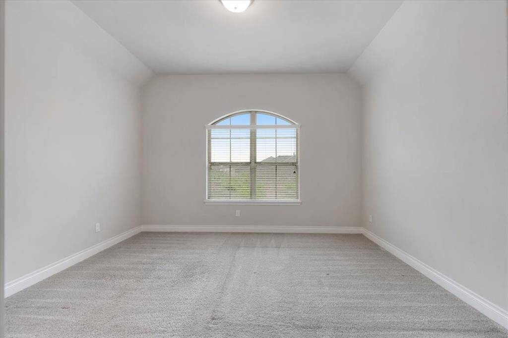 This photo shows a bright, empty room with neutral walls and carpet flooring. It features a large, arched window allowing natural light to fill the space, creating a welcoming atmosphere.