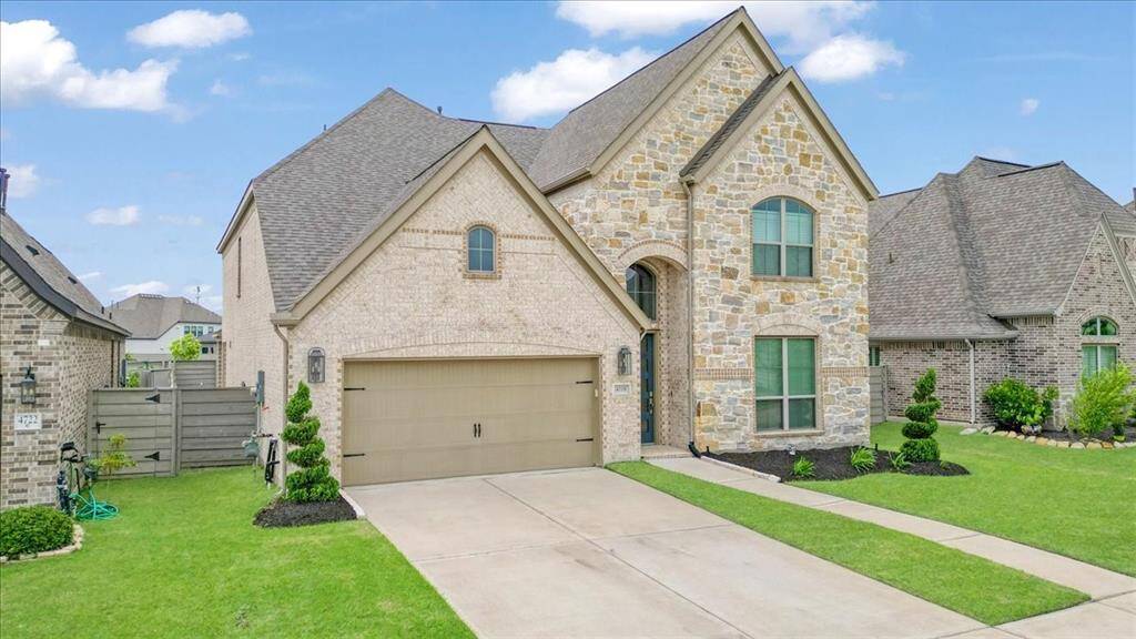 This is a modern two-story home with a mix of stone and brick exterior, featuring a two-car garage and a well-maintained lawn. The design includes large arched windows and a neatly landscaped front yard, creating an inviting curb appeal.