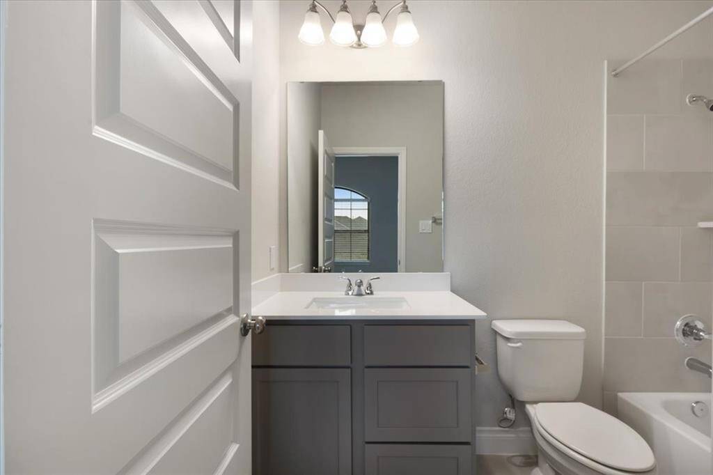 This photo shows a modern bathroom with a sleek vanity, large mirror, and overhead lighting. It features a toilet and a shower with a tiled wall, offering a clean and functional space.