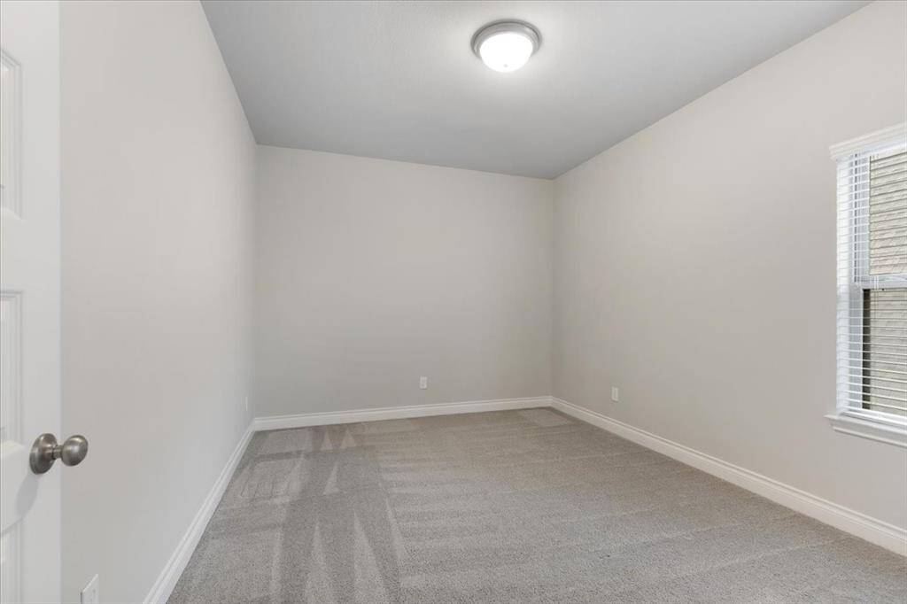 This room features neutral walls and carpeting, offering a clean and versatile space. It has a window for natural light and a central ceiling light fixture, ideal for use as a bedroom or office.