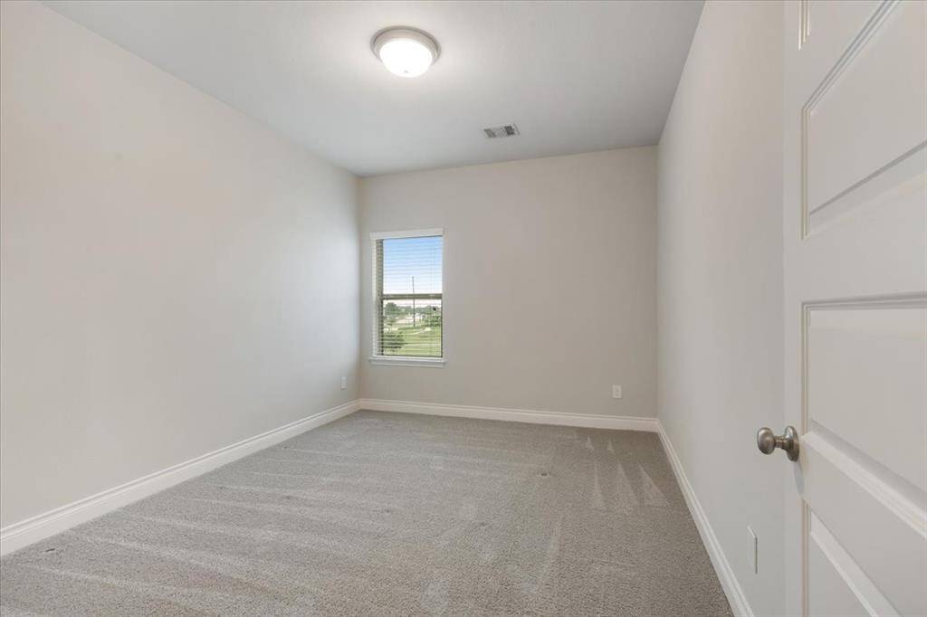 This room is a simple, well-lit space with neutral walls and carpet flooring. It features a single window allowing natural light and a ceiling light fixture. Ideal for use as a bedroom or office.