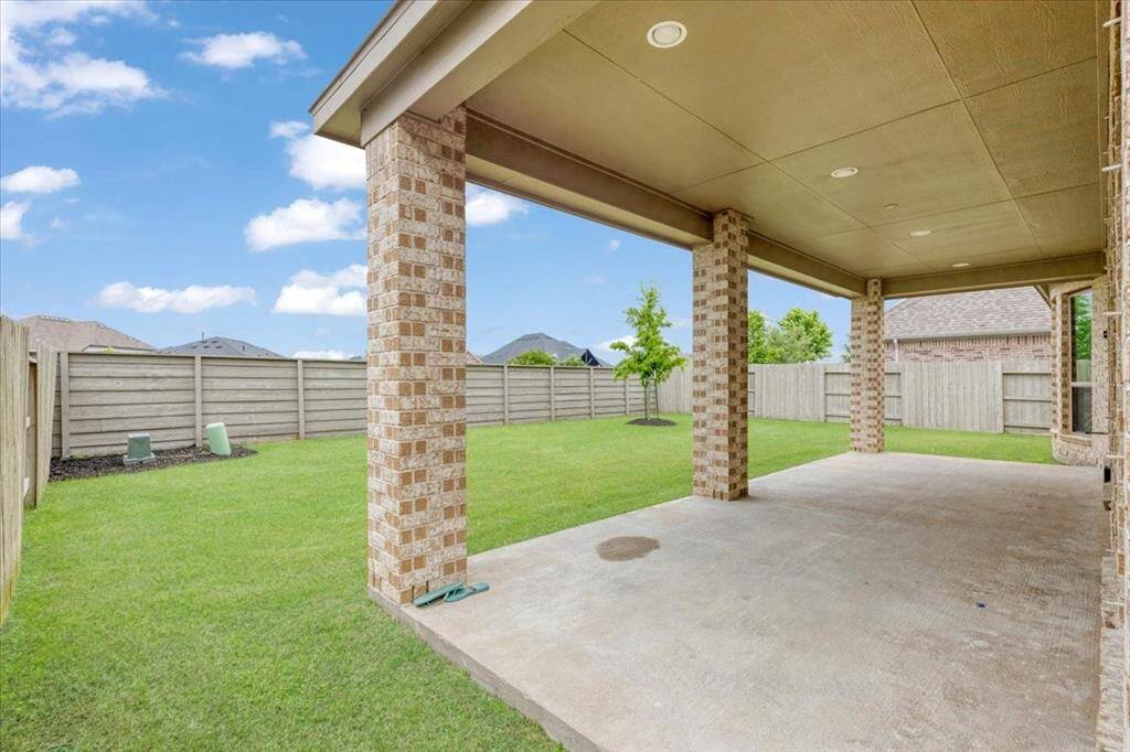 This photo showcases a spacious, covered patio with brick columns, overlooking a well-maintained, fenced backyard. Perfect for outdoor gatherings and relaxation.