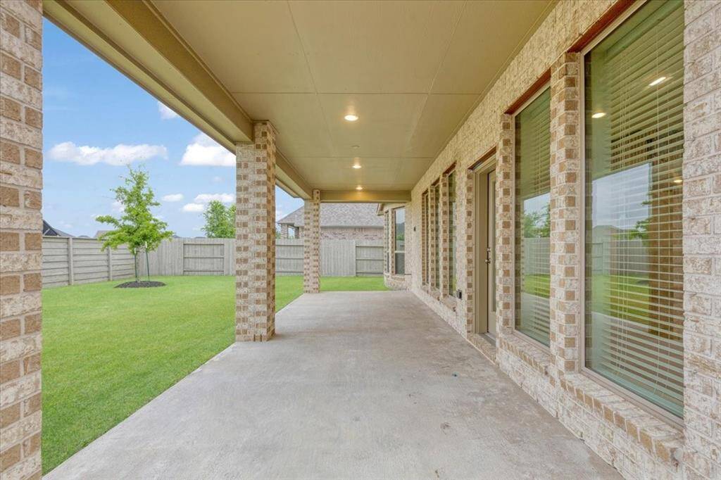 This photo showcases a spacious covered patio with brick pillars and large windows, overlooking a well-maintained, fenced backyard. Perfect for outdoor relaxation and entertaining.