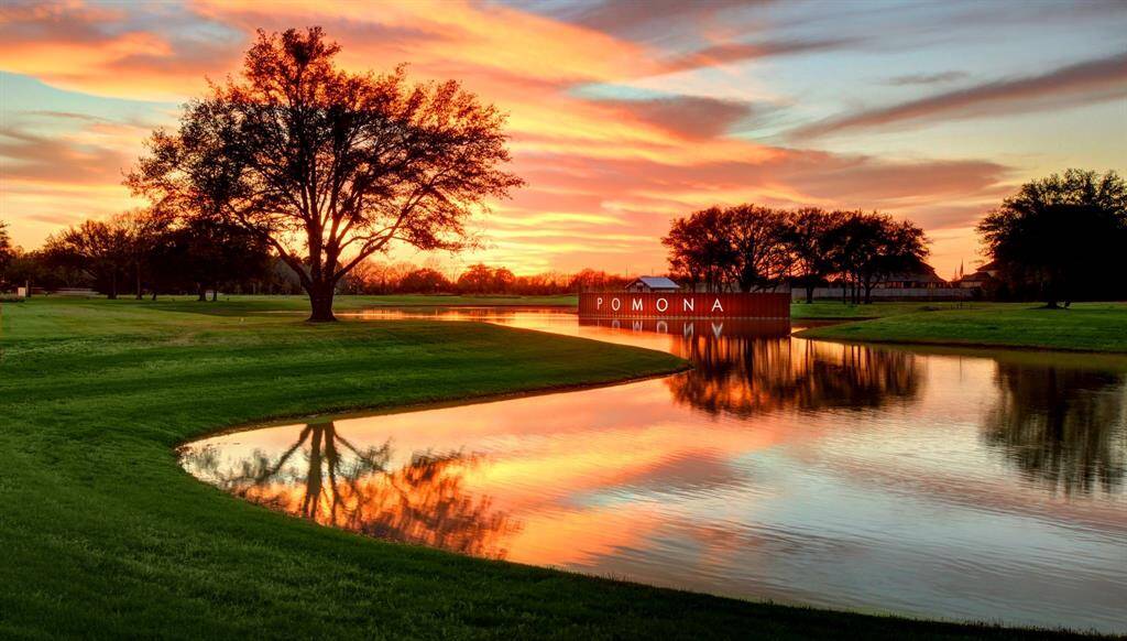 This photo showcases a serene lakeside view at sunset, with vibrant skies reflecting on the water. A lush green lawn and mature trees enhance the tranquil setting, marked with a welcoming "POMONA" sign. Ideal for those seeking picturesque surroundings.