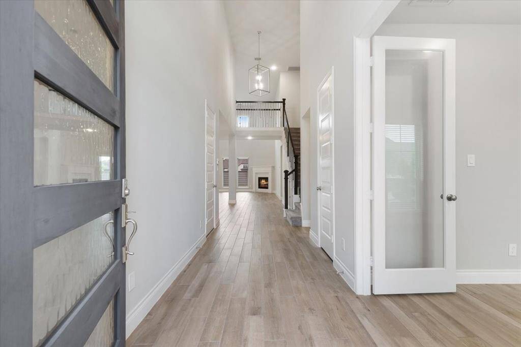 This photo showcases a bright, spacious entryway with light wood flooring and high ceilings. The hallway leads to a cozy living area with a fireplace, featuring modern finishes and a glass-paneled door on the right.