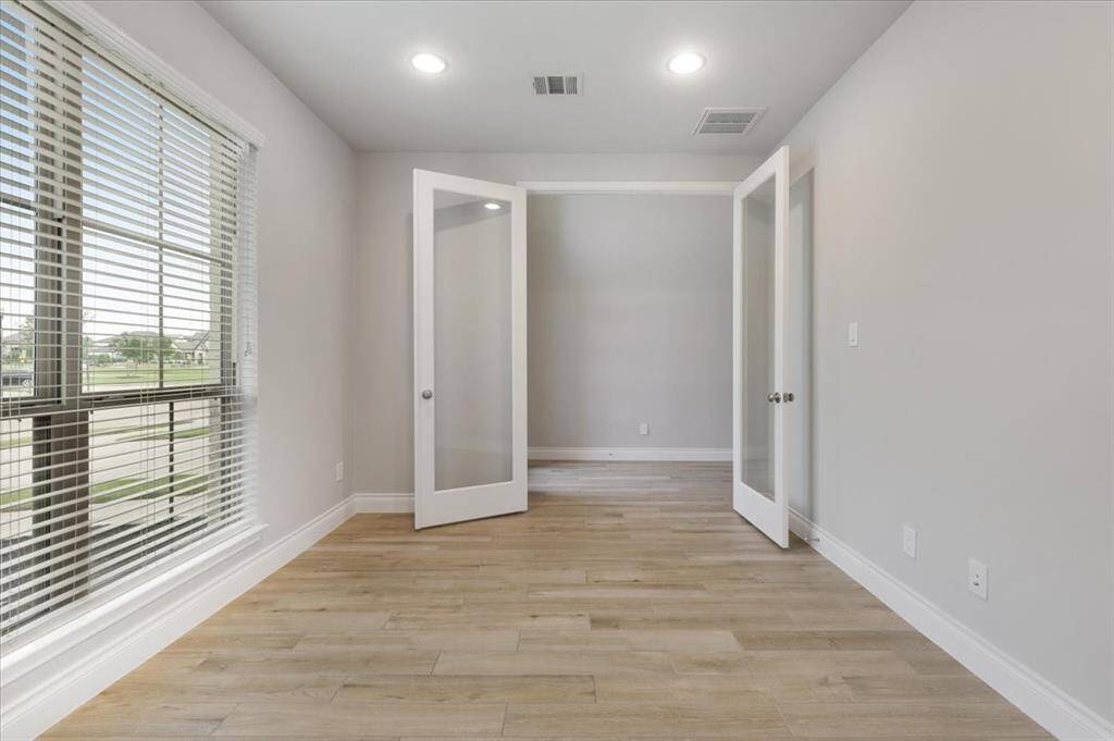 Bright room with large windows and wooden floors, featuring double glass doors leading to an adjacent space. Ideal for a home office or study.